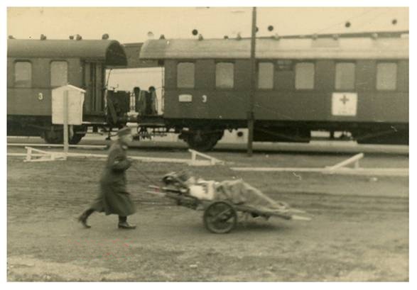 Transport of a wounded soldier on a two-wheeled stretcher; in the background a sanitary train............