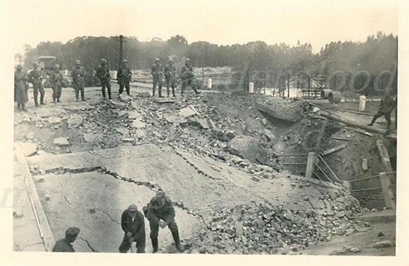 Several German soldiers are watching as a Polish civilian works at the damaged bridge ..................